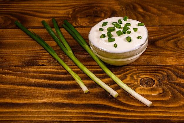 Bol en verre avec crème sure et oignon vert sur table en bois