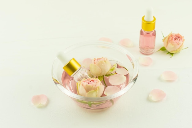 Bol en verre avec eau de rose, fleurs et pétales de rose, flacons cosmétiques à l'huile de fleur de zfir. aromathérapie, anti-stress.