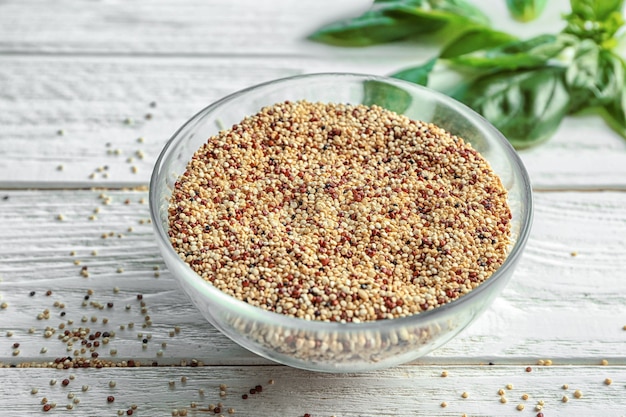 Bol en verre avec des grains de quinoa crus sur bois