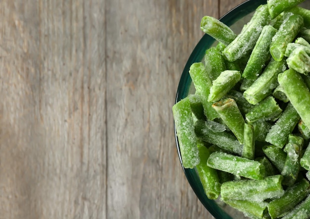 Bol en verre avec des haricots verts congelés sur fond de bois libre