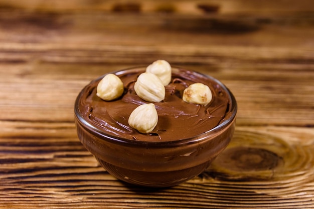 Bol en verre avec pâte à tartiner au chocolat et noisettes sur une table en bois