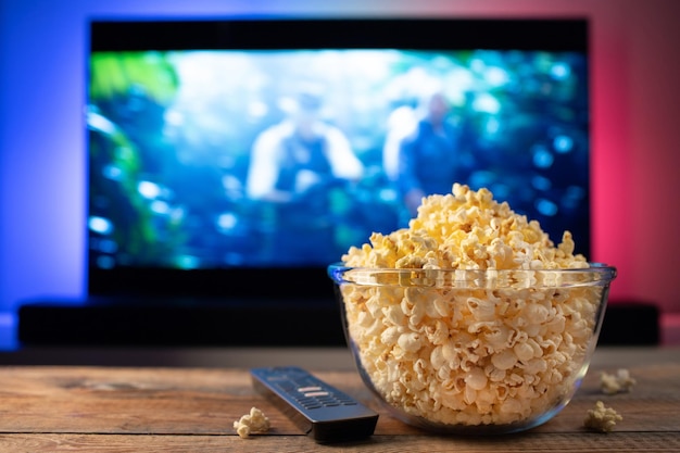 Un bol en verre de pop-corn et une télécommande en arrière-plan, la télévision fonctionne