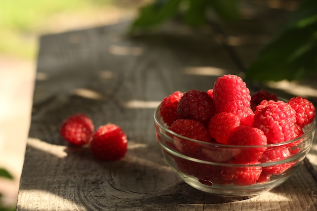 Bol en verre rempli de framboises sur une table de jardin en bois