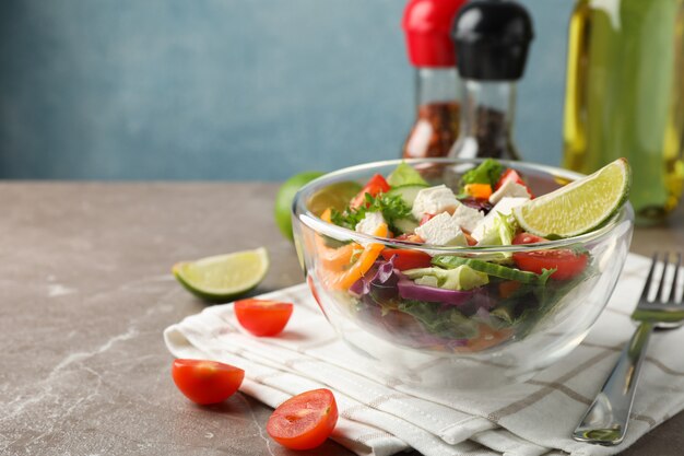 Bol en verre avec salade, serviette et épices sur fond gris