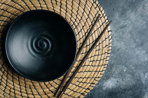 Bol vide noir (en céramique à la main) avec des baguettes chinoises sur une pierre grise