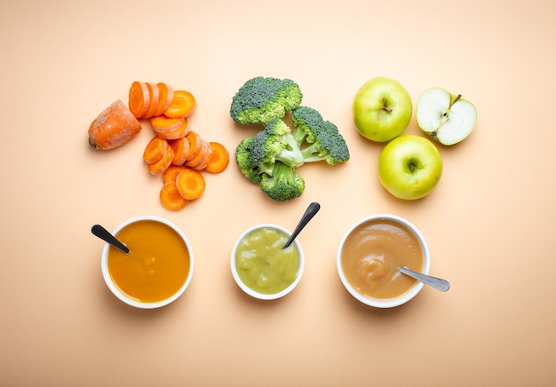 Bols blancs avec des aliments pour bébés naturels sains sur fond pastel. Purées, faites de fruits et légumes biologiques frais, flay lay, vue de dessus, concept. Nourriture pour enfants à base de carotte, brocoli, pommes