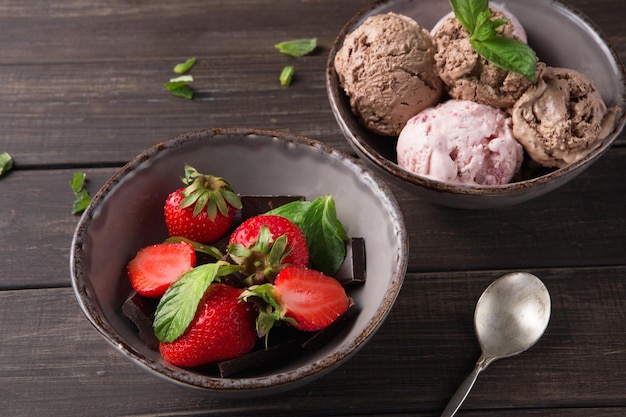 Bols de crème glacée au chocolat et aux baies et fraises sur fond de bois rustique avec feuilles de menthe et cuillère, gros plan. Dessert d'été fait maison