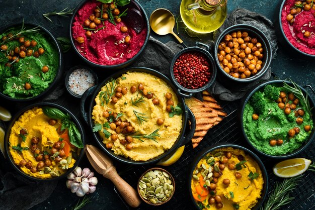 Photo bols de houmous colorés flatlay de diverses trempettes végétariennes houmous sur un fond noir en béton