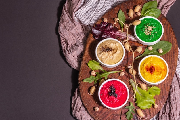 Bols de houmous colorés, trempettes végétaliennes saines. Cuisine traditionnelle du Moyen-Orient. Betteraves, épinards, épices aromatiques. Fond de béton de pierre noire, vue de dessus