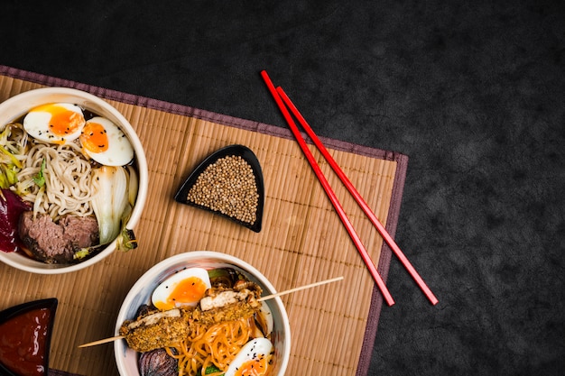 Photo bols de nouilles ramen aux œufs et légumes sur des baguettes sur le napperon sur fond noir