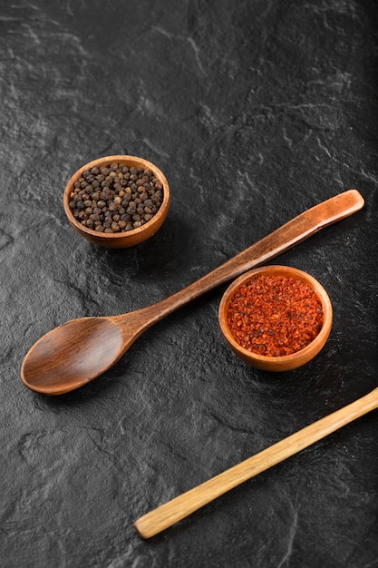 Bols de poivre de Cayenne rouge et grains de poivre sur une surface noire.