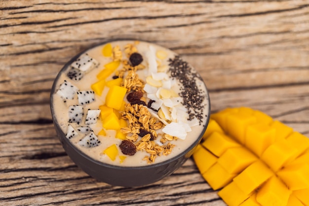 Bols de smoothie à base de granola banane mangue noix de coco râpée fruit du dragon graines de chia et menthe sur fond de bois vitamines fruits Concept