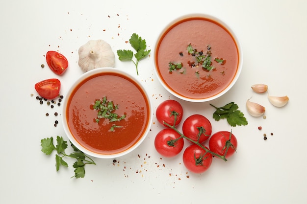 Bols avec soupe aux tomates et ingrédients sur blanc