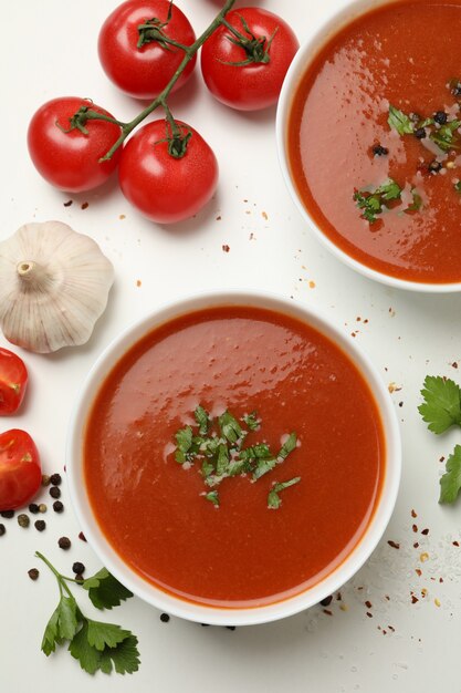 Bols avec soupe aux tomates et ingrédients sur blanc