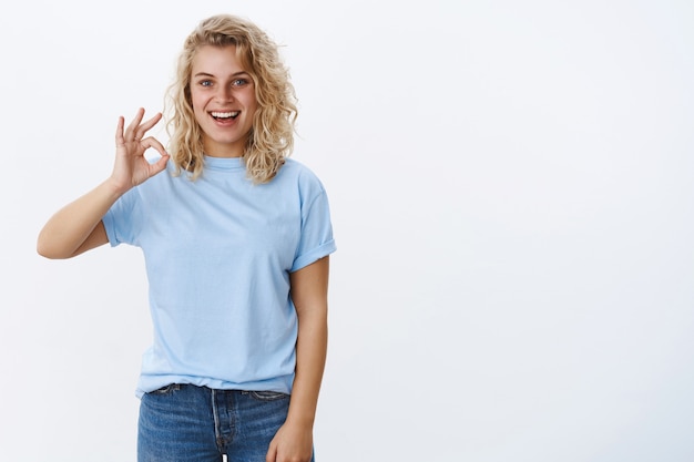 Bon j'approuve. Portrait d'une jeune femme séduisante excitée et ravie de 25 ans aux cheveux bouclés et aux yeux bleus souriant joyeusement et montrant un signe ok comme une idée géniale, recommande le produit