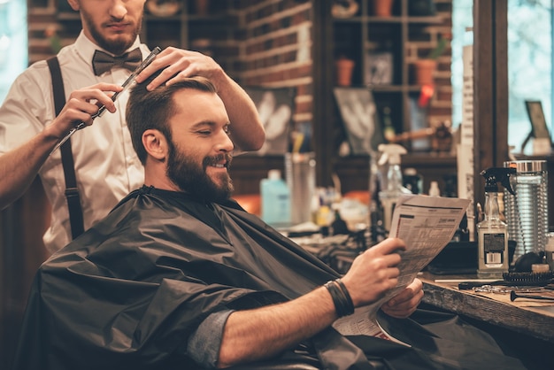 bon moment au salon de coiffure. joyeux jeune homme barbu se coupe les cheveux par le coiffeur