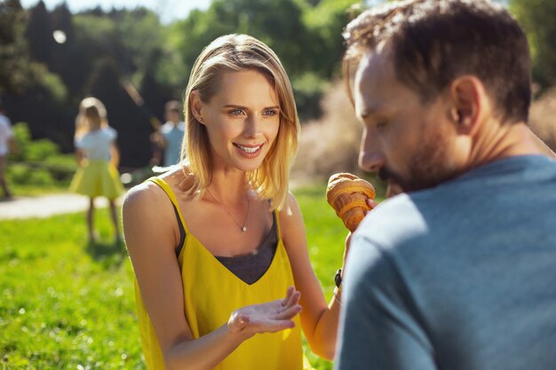 Bon moment. Joyeuse femme mince parlant avec son mari et leurs enfants jouant en arrière-plan