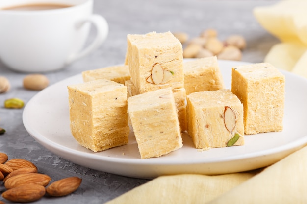 Bonbon indien traditionnel soan papdi en plaque blanche avec amande et pistache sur un béton gris.