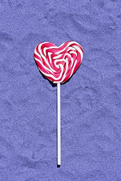 Bonbon sucette rouge en forme de coeur sur le sable plat vertical image tonique à la couleur tendance de l'année 2022 très peri