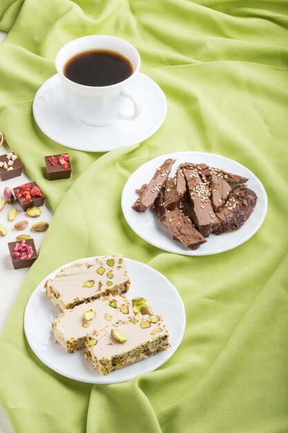 Bonbons arabes traditionnels halva de sésame avec du chocolat et de la pistache et une tasse de café sur une surface textile verte. vue de côté.