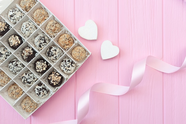 Bonbons artisanaux au chocolat sur table en bois rose. Boîte de chocolat ouverte avec deux coeurs et un ruban festif.