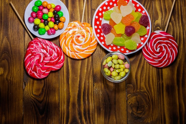 Bonbons au chocolat colorés, sucettes et bonbons gélifiés sur table en bois