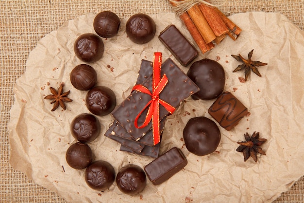 Bonbons au chocolat de différentes formes et barres de chocolat aux noix posées sur un morceau de papier en forme de coeur avec de l'anis étoilé et de la cannelle. Vue de dessus