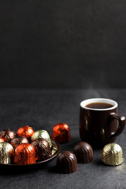 Bonbons au chocolat enveloppés dans une feuille multicolore et une tasse de café sur une surface noire