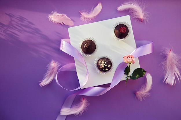 Bonbons au chocolat festifs vue de dessus avec des ombres. Plumes roses délicates et ruban violet