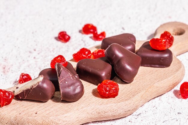 Bonbons au chocolat en forme de cœur avec des cerises séchées. Lumière dure moderne, ombre sombre. Un joli cadeau pour la Saint-Valentin ou un anniversaire. Fond de plâtre de tons clairs, place pour le texte