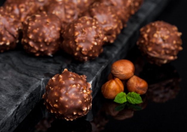 Bonbons au chocolat de luxe avec des morceaux de noisettes et des feuilles de menthe sur une table en marbre noir.