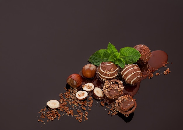 Bonbons au chocolat ronds avec des noix de remplissage douces et des feuilles de menthe sur un fond sombre avec réflexion