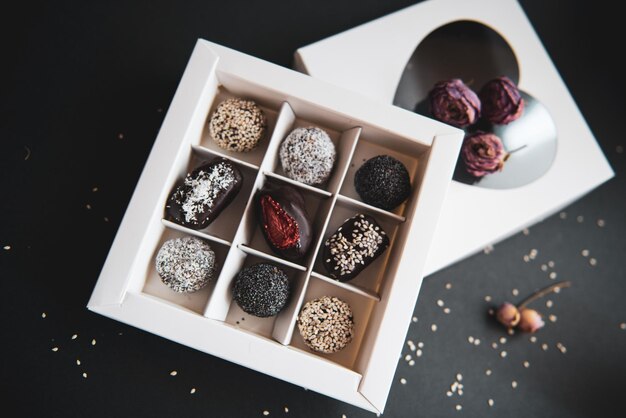 Photo des bonbons aux fruits et au chocolat faits à la main sans sucre et sans gluten dans une boîte blanche et un fond noir