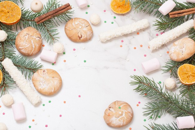 Bonbons et biscuits avec des branches d'arbres de Noël sur fond de marbre blanc