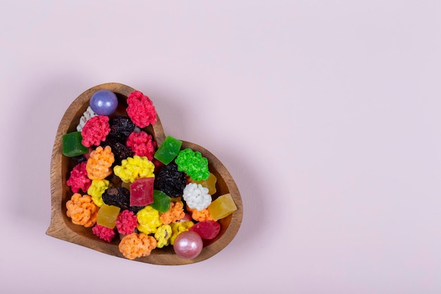 Des bonbons et des bonbons colorés sont versés dans un vase en bois en forme de cœur