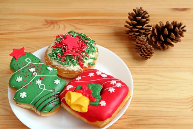 Bonbons colorés décorés de Noël sur une assiette blanche servis sur une table en bois avec des pommes de pin sèches