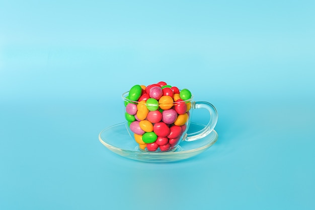 Bonbons colorés glacés. Mug en verre sur une soucoupe remplie de chocolats colorés en forme de bouton