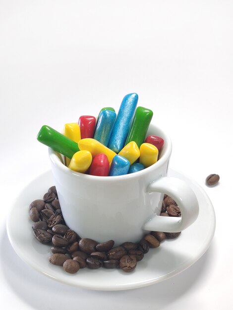 Bonbons colorés moelleux dans une tasse sur un mur blanc