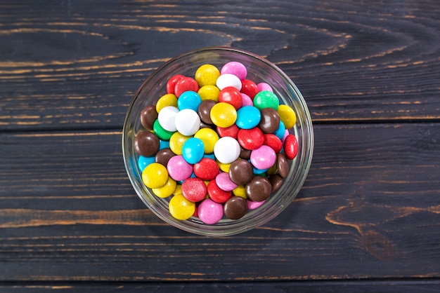 Bonbons colorés ronds dans une assiette sur une surface en bois.