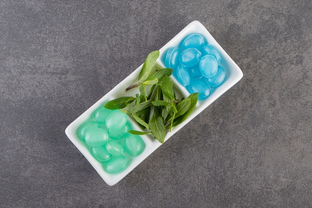 Bonbons durs bleus et verts dans un bol placé sur une table en pierre.