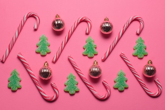 Des bonbons en forme d'arbre de Noël et de boules dorées se trouvent sur un fond rose, vue de dessus. Notion de Noël et nouvel an