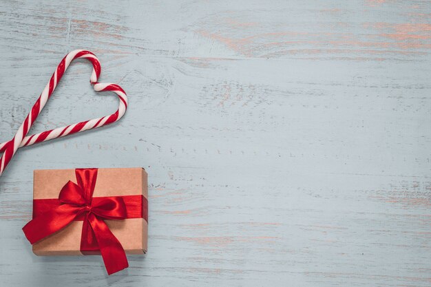 Bonbons en forme de coeur et un cadeau d'artisanat avec ruban rouge sur un fond en bois peint clair. Vue d'angle de côté supérieur, pose à plat. Concept de la Saint-Valentin. Copyspace.