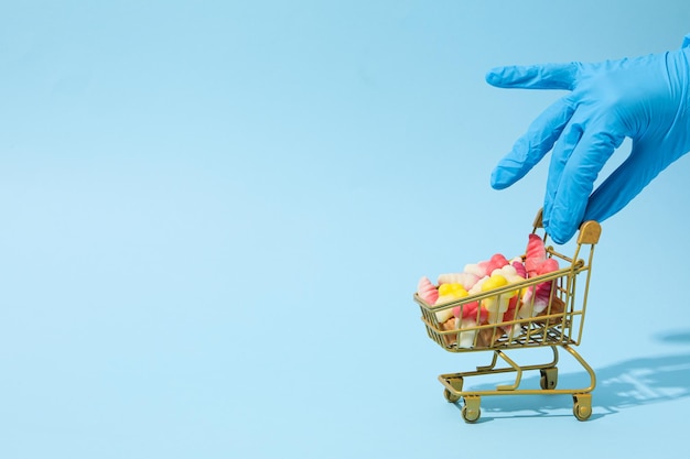 Bonbons à la gelée dans un caddie et main dans un gant médical sur fond bleu espace pour le texte