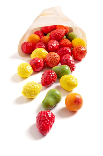 Bonbons gommeux colorés aux fruits dispersés dans un sac en papier sur fond blanc. Vue verticale