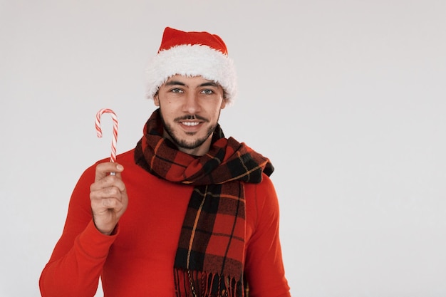 Avec des bonbons Jeune bel homme en vêtements de nouvel an debout à l'intérieur sur fond blanc