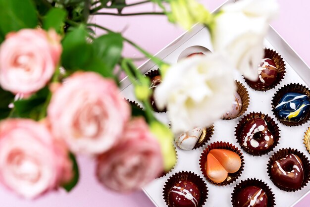 Bonbons de luxe peints avec différentes couleurs dans une boîte blanche sur fond rose Beaux et exclusifs bonbons au chocolat faits à la main
