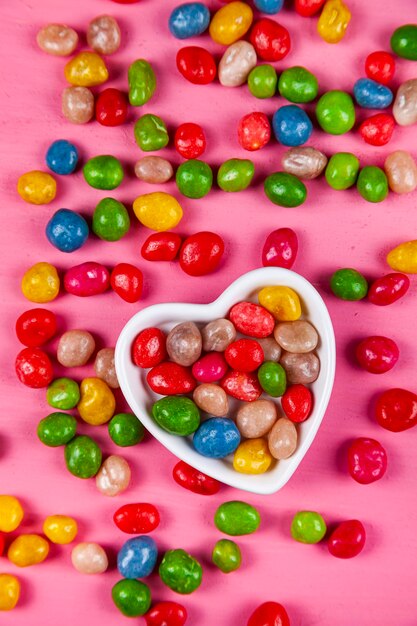 Bonbons multicolores dans une assiette en forme de coeur sur fond de bois rose. La Saint-Valentin.