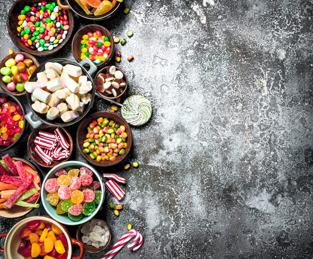 Bonbons multicolores, gelée et guimauves dans un bol. Sur un fond rustique.