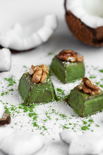 Bonbons à la noix de coco avec du chocolat et du thé matcha sur un fond en bois clair