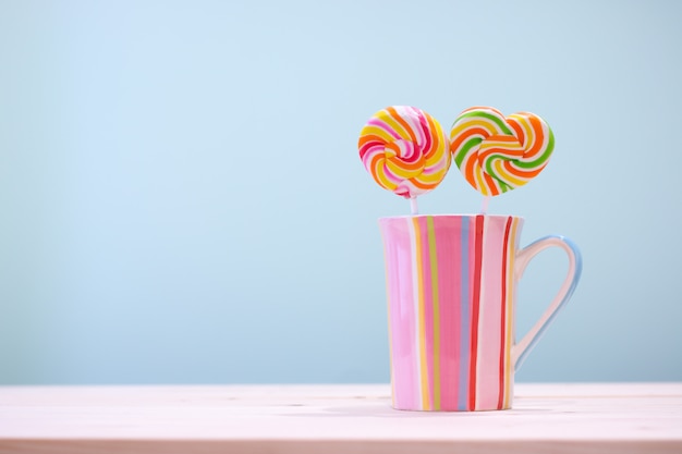 Bonbons ronds colorés et bonbons coeur dans une coupe de rayures verticales couleur pastel sur table en bois